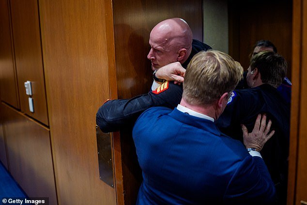 धक्कादायक क्षण एक अमेरिकन सिनेटर काँग्रेसच्या सुनावणीतून ओरडणाऱ्या मरीनला एस्कॉर्ट करण्यासाठी कॅपिटल पोलिसात सामील झाला